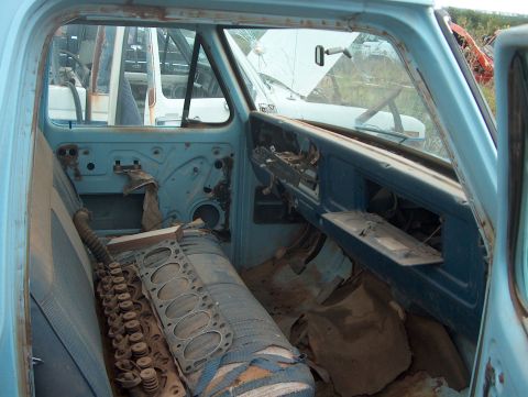 1979 Ford Bronco - The interior of a dilapidated truck cab, showing worn seats and a disassembled engine block, with other vehicles visible outside.