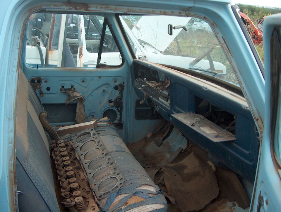 Interior of a light blue truck cab with ripped seats and a disassembled engine block on the passenger side