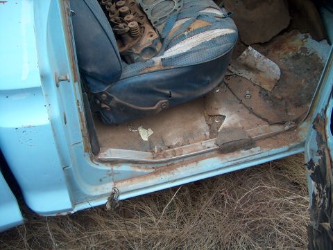 1979 Ford Bronco - The interior of a light blue vehicle shows a worn seat and significant rust on the floor, indicating disrepair.