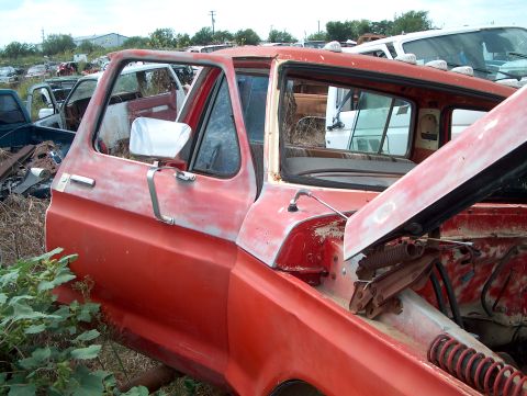 1979 Ford Bronco - Junkyard scene the side of a red pickup truck cab with its hood open.