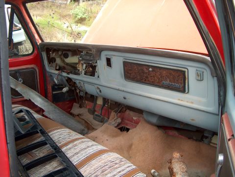1979 Ford Bronco - The interior of a 1979 Ford Bronco shows its aged dashboard with woodgrain trim and a striped bench seat.