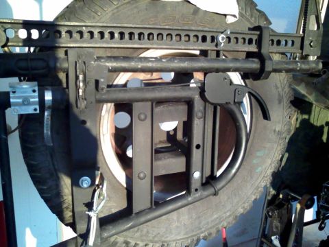 1992 Ford Bronco - Close-up of a modified spare tire carrier, a Hi-Lift jack and various mounting hardware.