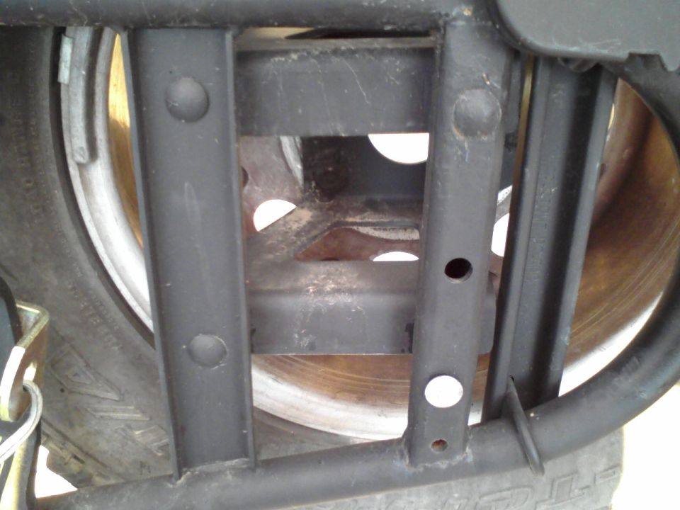 Close-up of a black metal spare tire carrier with a tire and brake rotor visible
