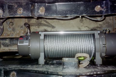 1988 Ford Bronco - Close-up of a vehicle winch and its steel cable, mounted to the frame.