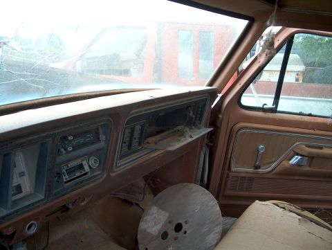 1979 Ford Bronco - The interior of a weathered vehicle shows a dusty dashboard and door panel, with another vehicle visible outside.