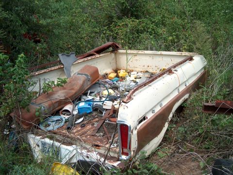 1979 Ford Bronco - A derelict pickup truck bed, likely from the late 1970s, sits abandoned and filled with various discarded items.