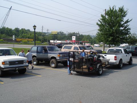 1984 Ford Bronco - Several vehicles, including a Ford Bronco and a pickup truck with a trailer, are parked in a lot near a gas station.