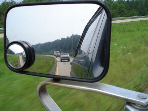 1984 Ford Bronco - Reflection in the side mirror shows vehicles traveling on a highway with trees and hills in the background.