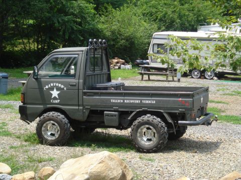1984 Ford Bronco - Modified mini truck with off-road tires and custom markings is parked near a camper.