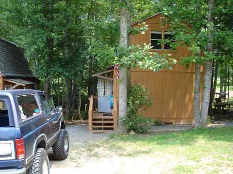 1984 Ford Bronco - A dark blue SUV with lifted suspension is parked in front of a rustic wooden cabin in a wooded area.