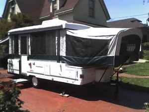 1995 Ford Bronco - A pop-up camper trailer is parked in a driveway with its awning extended.