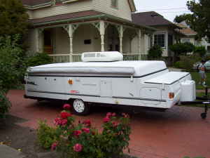 1995 Ford Bronco - A white pop-up camper trailer is parked on a red brick driveway in front of a house.
