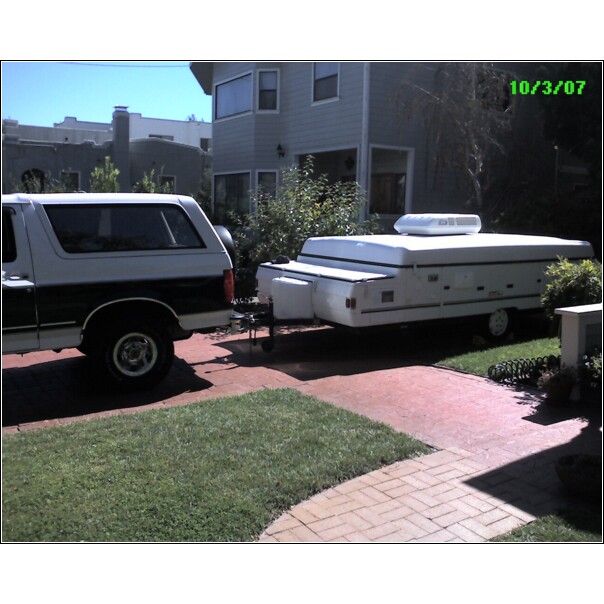 Two-tone Ford Bronco towing a white pop-up camper, rear view