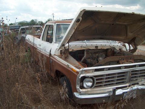 1979 Ford Bronco - A weathered Ford pickup truck sits abandoned in a field of dry grass, its hood propped open to reveal the engine.