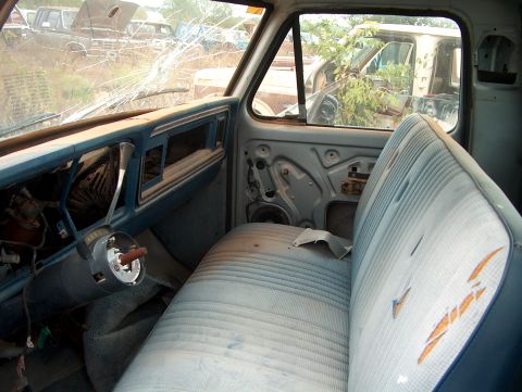1979 Ford Bronco - Interior view of a 1979 Ford Bronco in a junkyard, showing worn blue seats and a heavily cracked windshield.