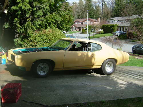 Yellow primer coupe with teal hood, side view in driveway
