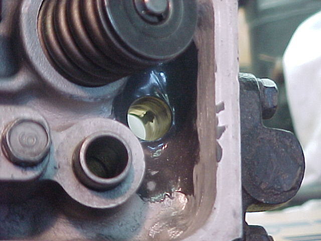 Close-up of cylinder head interior showing valve spring, rocker arm, and brass valve guide through an opening
