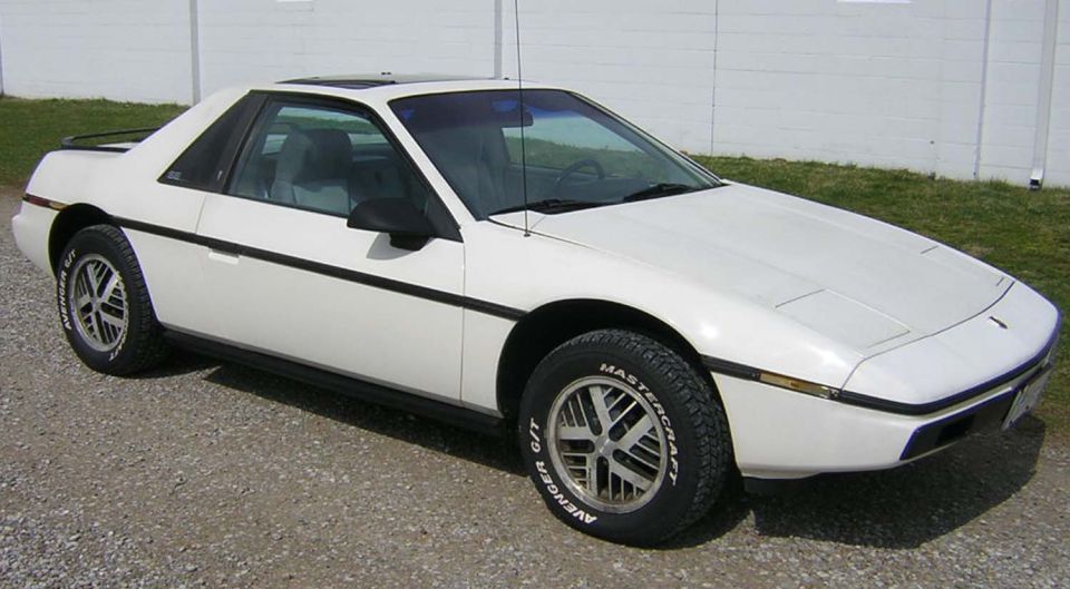 White Pontiac Fiero parked on gravel, side view