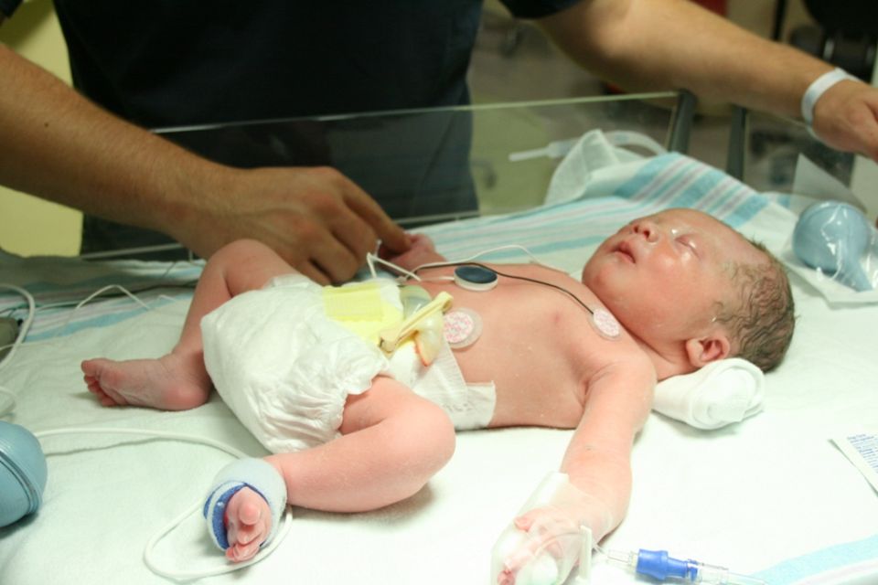 Newborn baby with medical monitoring equipment in an incubator
