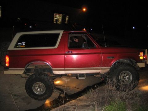 1995 Ford Bronco - A red 1995 Ford Bronco with a white top is seen from the side at night.