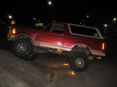 1995 Ford Bronco - This red SUV is shown off-roading at night, with its tires angled on a rocky surface.
