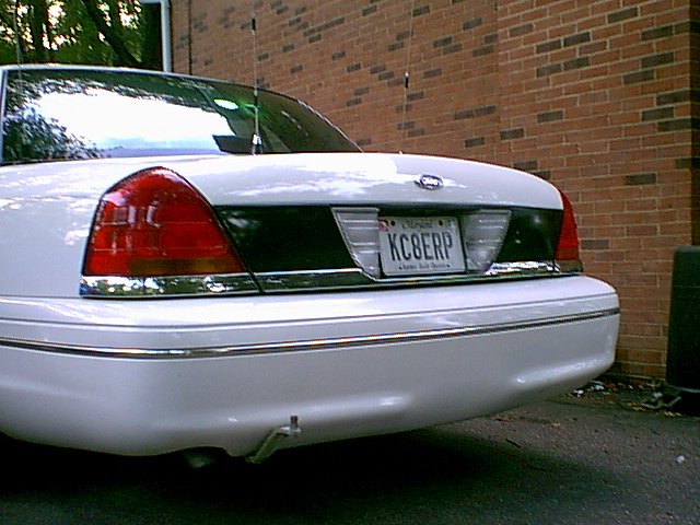Rear of white Ford Crown Victoria with plate KC8ERP and trailer hitch, parked by brick wall