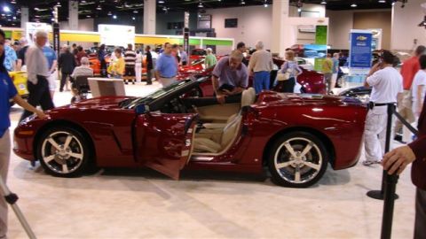 1996 Ford Probe - A red convertible sports car is displayed with its doors open at an auto show, attracting attention from attendees.