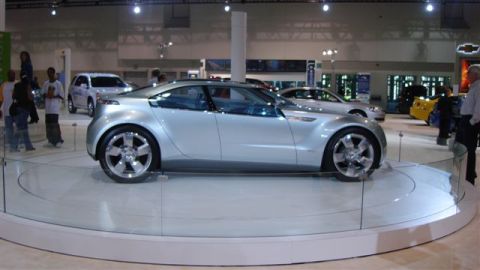 1996 Ford Probe - A futuristic silver concept car is showcased at an auto exhibition with other vehicles in the background.