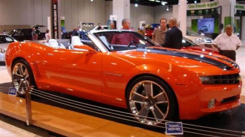 1996 Ford Probe - An orange convertible sports car with a white interior is on display at an auto show.