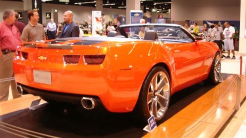 1996 Ford Probe - An orange convertible sports car is displayed at an auto show, a design and custom wheels.