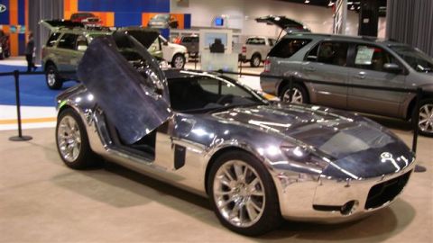 1996 Ford Probe - A custom chrome sports car with butterfly doors is displayed at an auto show, with other vehicles visible in the background.