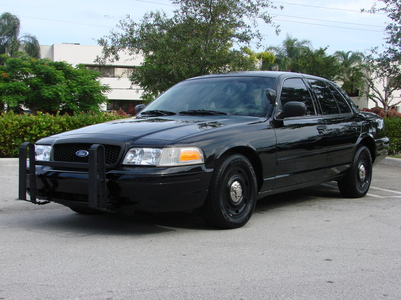 Black Ford Crown Victoria police car with a push bumper, parked on asphalt