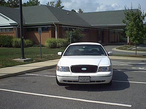 1998 Ford Crown Victoria - A white sedan is parked in a lot in front of a building. The license plate is visible.