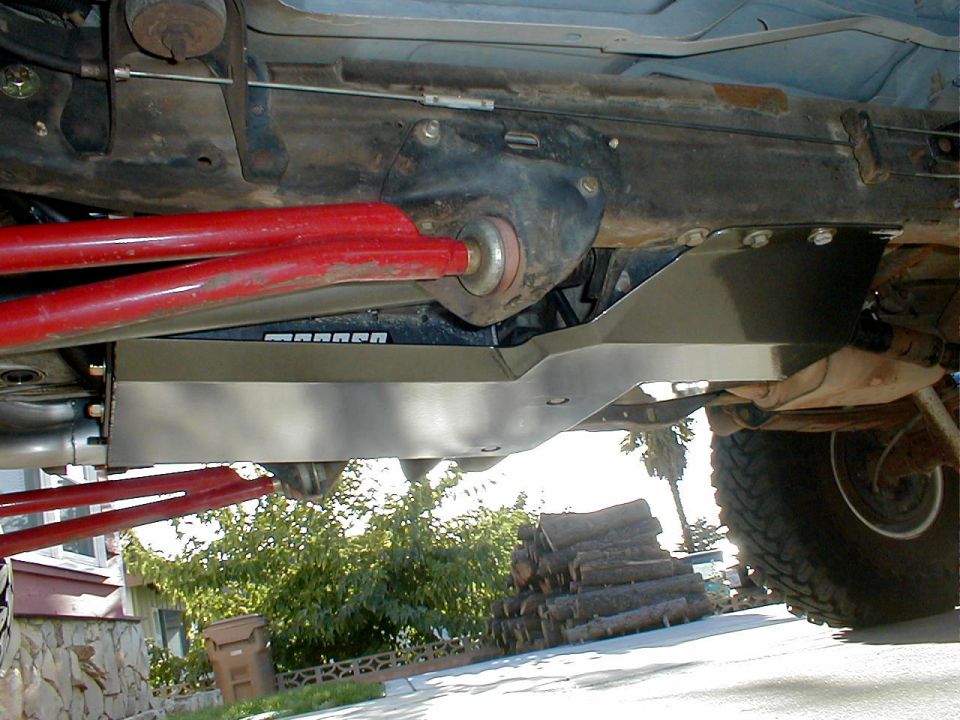 Underbody skid plate and red suspension arms on a vehicle. Some text is visible on the skid plate