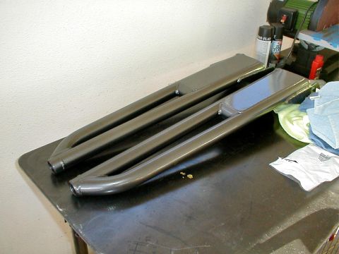 1996 Ford Bronco - Two metal running boards are resting on a dark surface, possibly before installation.