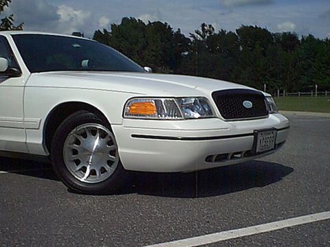 1998 Ford Crown Victoria - The front quarter panel and grille of a white 1998 Ford Crown Victoria are visible.