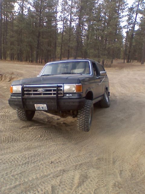 1988 Ford Bronco - Front three-quarter view of a dark full-size Ford Bronco with hardtop, a tube grille guard over the Ford-badged grille and a 4x4 fender emb…
