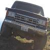 1988 Ford Bronco - This Ford Bronco is shown from the front, angled upwards on a dirt path with vegetation visible below.