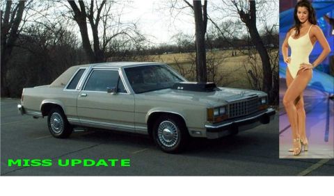 1985 Ford LTD Crown Victoria - A silver-beige 1980s Ford full-size two-door coupe with a padded vinyl half-roof, wire-spoke wheel covers and a black hood scoop marked "5.…