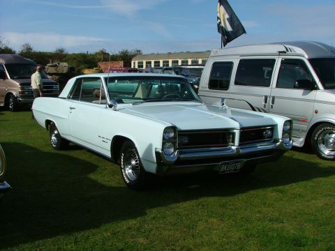 1988 Ford Sport - A light blue 1965 Pontiac Catalina coupe is parked on a grassy field next to a white van.