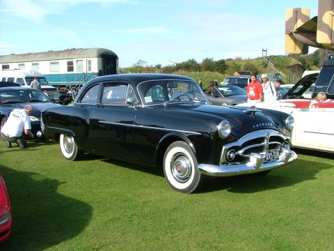 1988 Ford Sport - A classic black Packard sedan is displayed on a grassy field, with a train and other vehicles in the background.