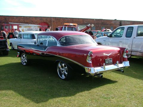 1988 Ford Sport - A classic two-tone Chevrolet coupe is parked on the grass with other vehicles and buildings in the background.