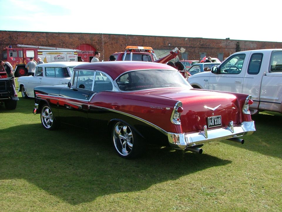 Two-tone red and black 1956 Chevrolet Bel Air coupe, rear view. Other cars and fire trucks in background