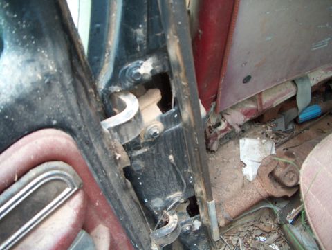 1979 Ford Bronco - Interior view of a vehicle's door hinge and worn seat fabric, with debris on the floor.