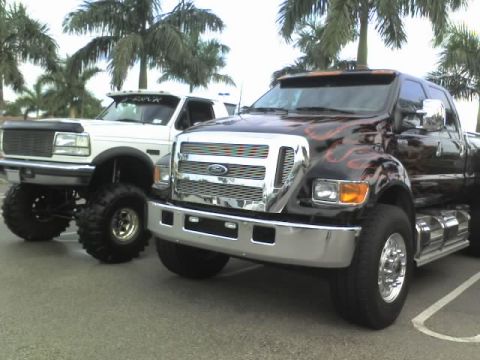 1995 Ford Bronco - Two custom Ford trucks are parked side-by-side, with one flame graphics and the other a lifted stance.