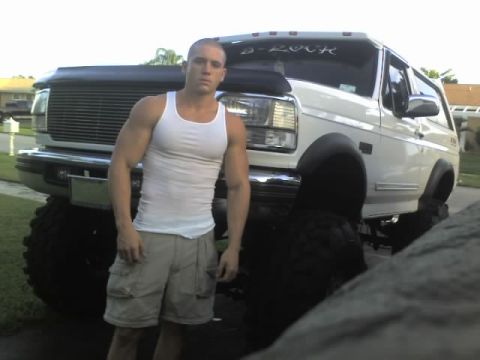 1995 Ford Bronco - A man poses in front of a heavily modified white Ford Bronco with oversized tires.