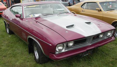 1991 Ford Bronco - A maroon Ford Falcon coupe with silver hood stripes is parked on grass next to a gold car.