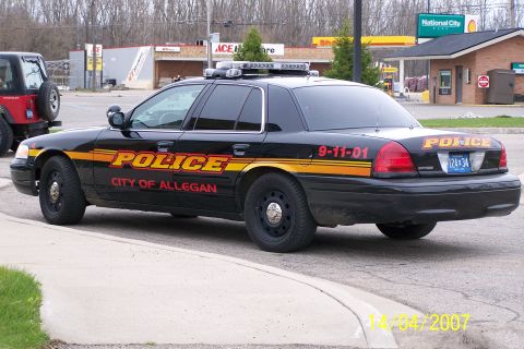 2003 Ford Crown Victoria - A black police car with 'POLICE' and 'CITY OF ALLEGAN' text is parked on the street.