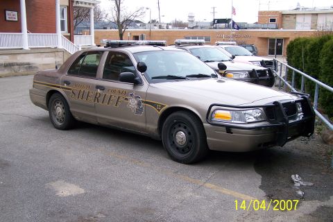2003 Ford Crown Victoria - A tan 2003 Ford Crown Victoria Police Interceptor, marked "WHEELER COUNTY SHERIFF", is parked alongside other police vehicles.