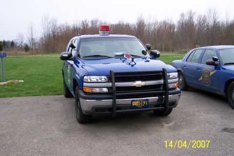 2003 Ford Crown Victoria - Two blue police vehicles, a Chevrolet Tahoe and a Ford Crown Victoria, are parked side-by-side on a paved surface.